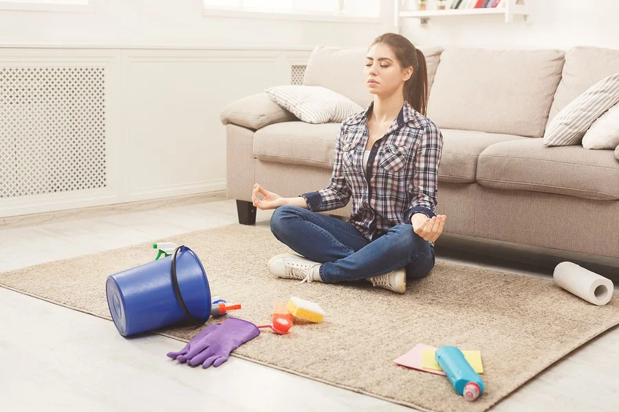 Woman Meditating, Sitting On Carpet While Cleaning Home In The L person meditating on clean rug