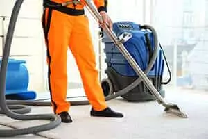 Technician wearing safety uniform, using a vacuum to clean a carpet